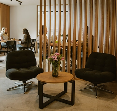 Eingangsbereich des Hotels zwölf87 – Traumwerk in Ravensburg mit zwei modernen Sesseln und einem kleinen Tisch im Vordergrund, im Hintergrund sitzen Menschen an Tischen und unterhalten sich