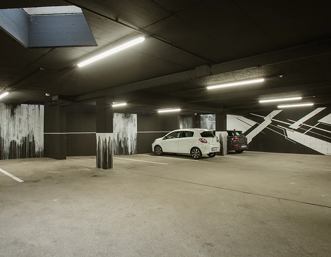 Tiefgarage des Hotels zwölf87 – Traumwerk in Ravensburg mit einem weißen und einem schwarzen Auto, die nebeneinander geparkt sind
